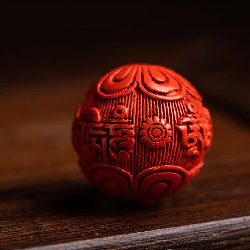 Single carved red cinnabar bead with engraved Om Mani Padme Hum sacred symbols on wooden surface