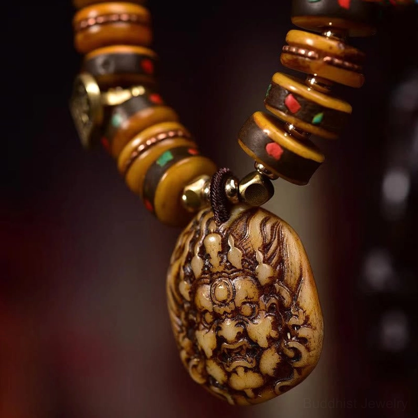Detailed view of carved wrathful deity Buddhist pendant with brown bone beads and metal connecting clasp
