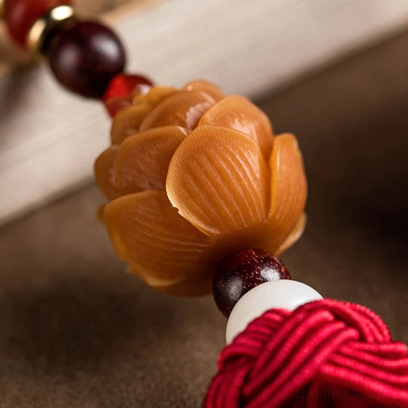 Carved wooden lotus bead charm with polished lotus shape, reddish-brown sandalwood beads, and red rope tassel in extreme close-up