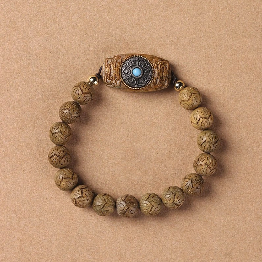 Carved wooden prayer bracelet with round beads and ornate turquoise centerpiece, overhead view