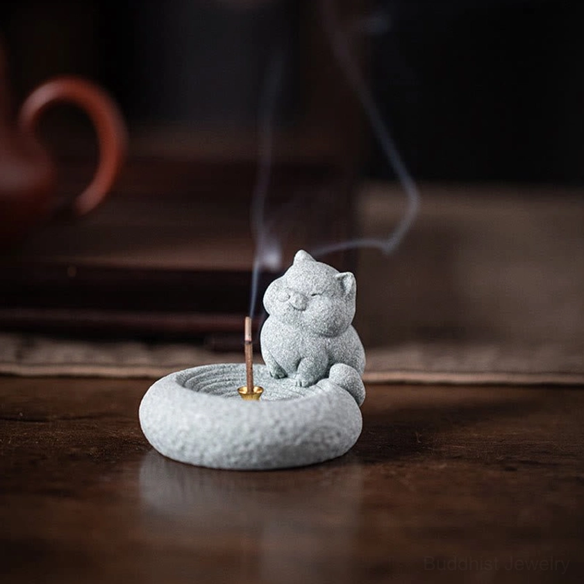 Close-up sitting cat incense burner with golden socket and burning incense on tea table