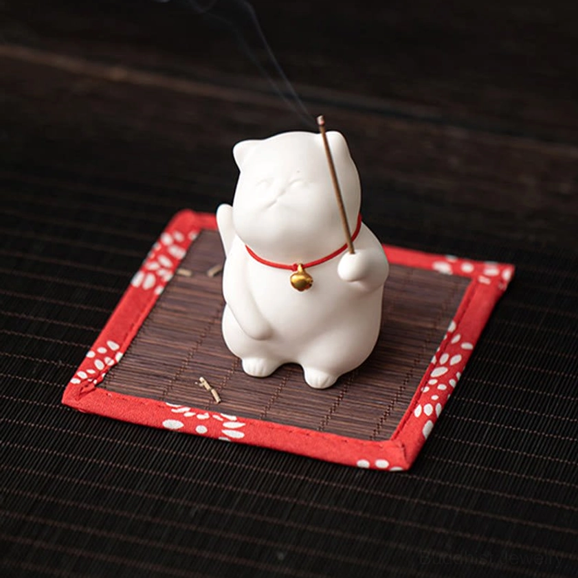 Ceramic cat incense stand with square woven red-bordered mat on striped desk surface, smoking incense