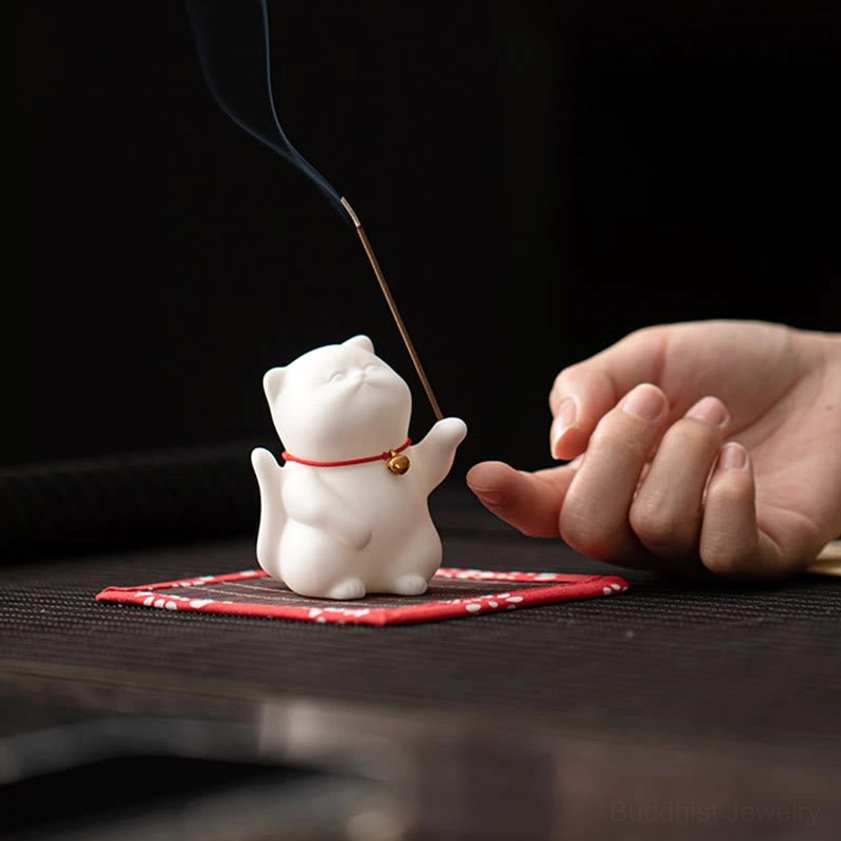 Ceramic cat incense burner with red-trimmed bamboo mat showing lit incense stick with rising smoke