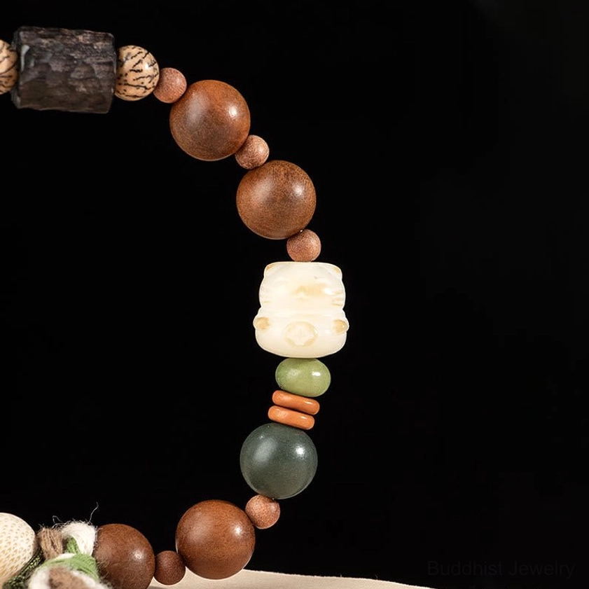 Close-up detail of carved cat paw charm and dark wood spacer beads on elastic bracelet with green accent stones