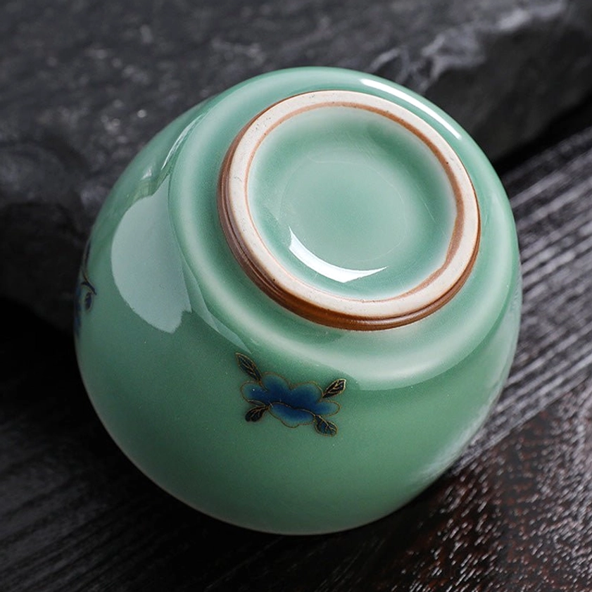 Complete celadon Buddhist tea cup with base showing unglazed ceramic foot rim and hand-painted motif artistry