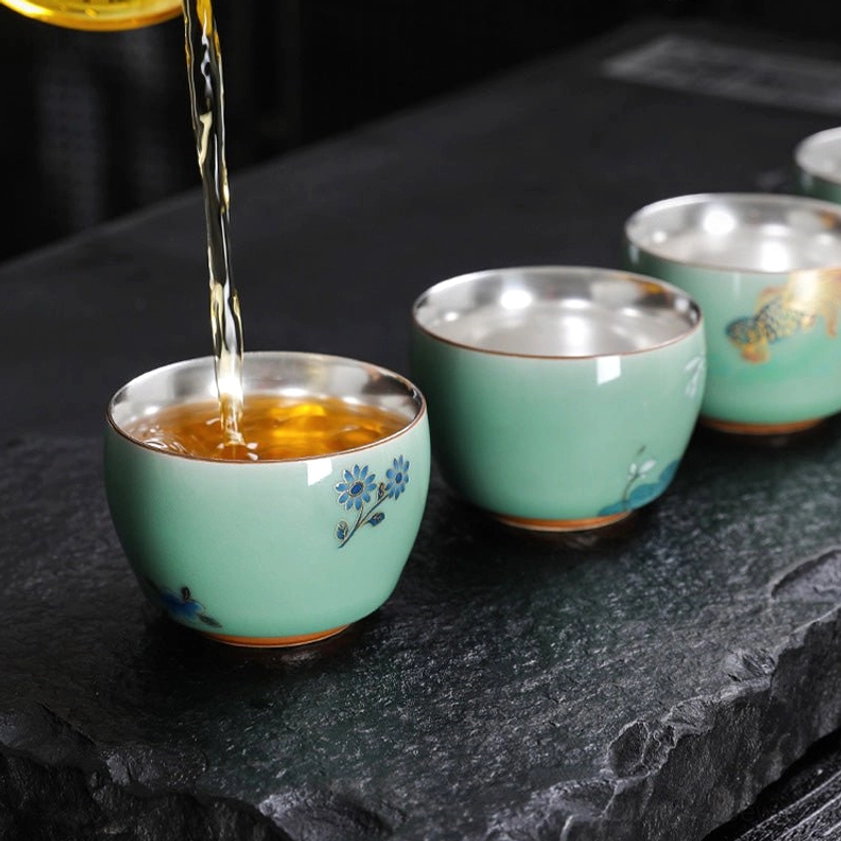 Set of multiple celadon Buddhist tea cups with varied butterfly lotus and koi fish designs grouped together
