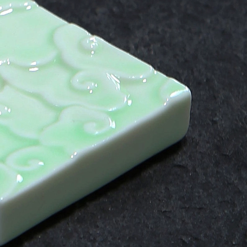 Low-angle side view of celadon ceramic incense holder against dark stone backdrop, highlighting 3D embossed cloud pattern and glossy glazed surface