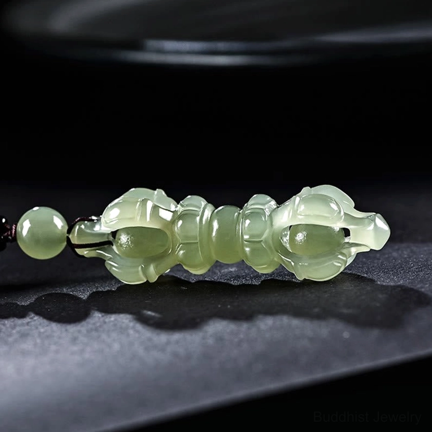 Celadon Hetian jade Dorje Vajra pendant necklace flat lay on dark matte surface, displaying translucent jade texture and hollow carving