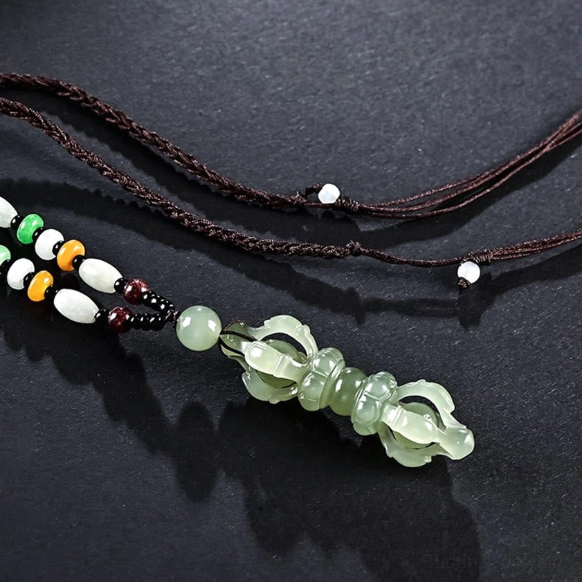Celadon Dorje Vajra jade pendant with multicolor beaded braided lanyard on dark matte surface, low oblique angle view