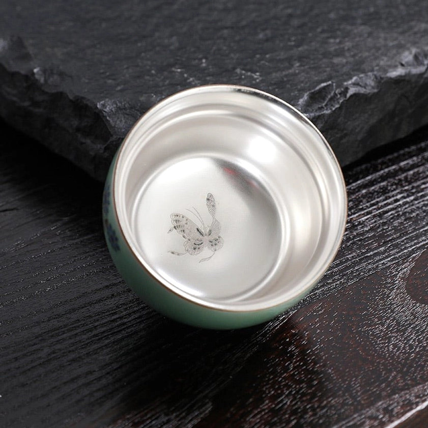 Interior overhead view of celadon tea cup showing hand-painted butterfly artwork and lustrous silver-lined inner surface