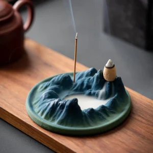 Buddhist ceramic backflow incense burner with mountains and river design on wooden tea table, showing matte ceramic finish with teal base and indigo mountain surface