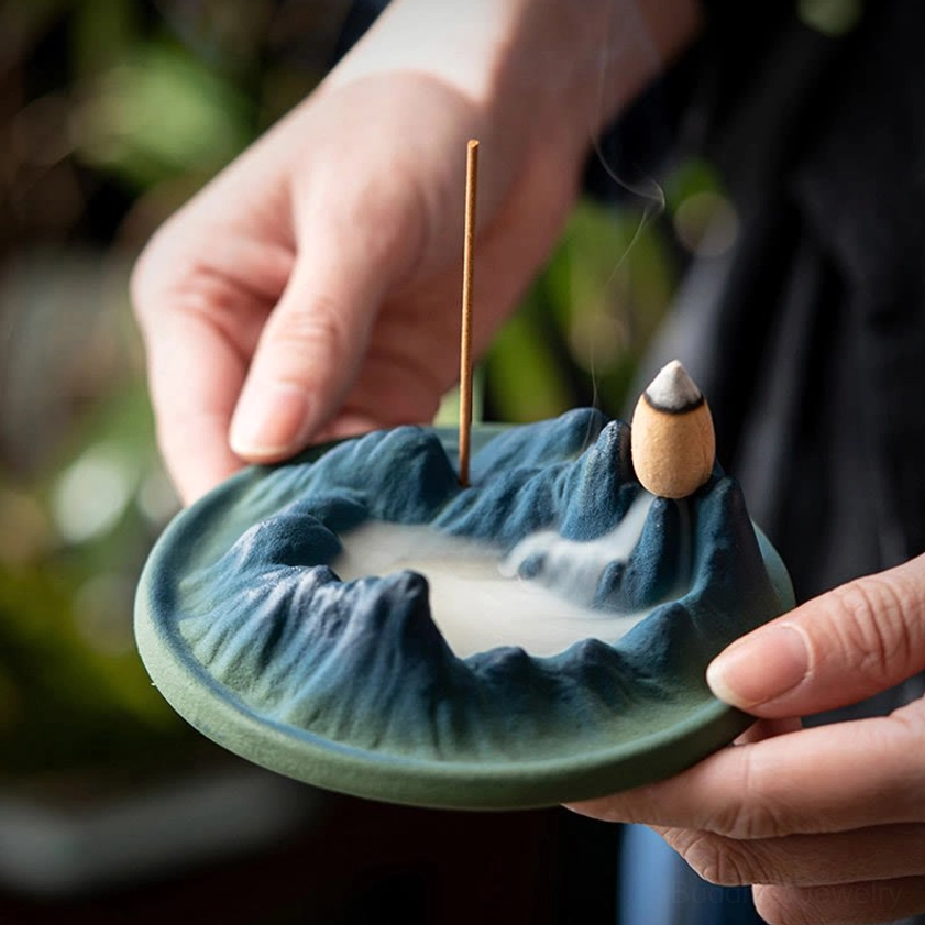 Handheld Buddhist ceramic incense holder being held in two hands with incense stick, perfect for meditation room or personal ritual