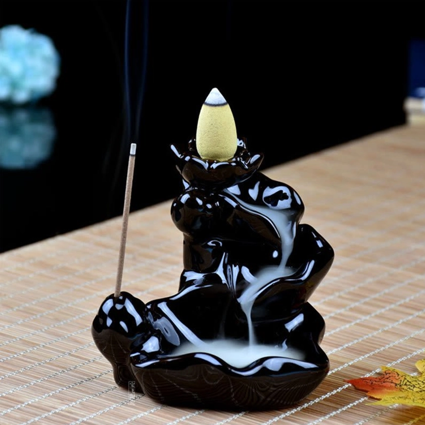 Ceramic backflow incense burner with yellow incense cone burning, glossy black finish on bamboo mat