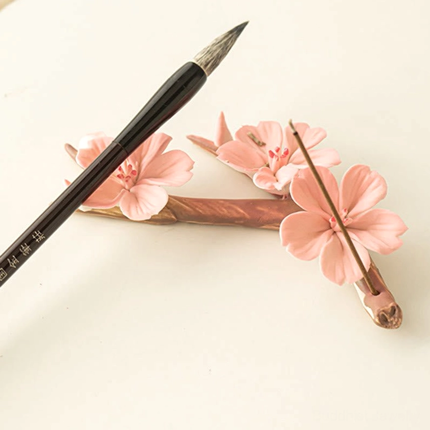 Ceramic plum blossom incense holder with resting incense stick and Chinese calligraphy brush, artistic desktop arrangement