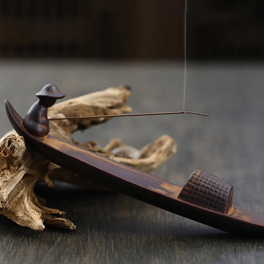 Artisan ceramic fisherman boat incense burner placed on driftwood with long smoking incense stick