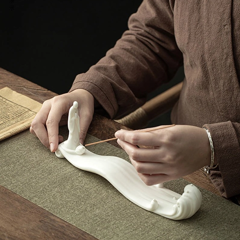 Adjusting incense stick in handcrafted white ceramic Buddhist incense holder close-up detail