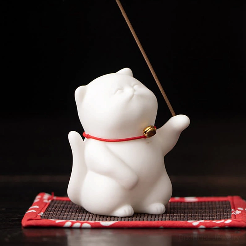 Cat-shaped ceramic incense burner on red-trimmed bamboo mat with smoking incense stick, front low angle