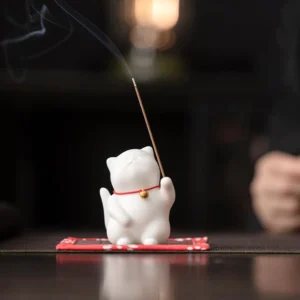 White ceramic cat incense burner with red collar and gold bell displayed on floral tatami coaster with burning incense stick, ideal for meditation and mindfulness practice