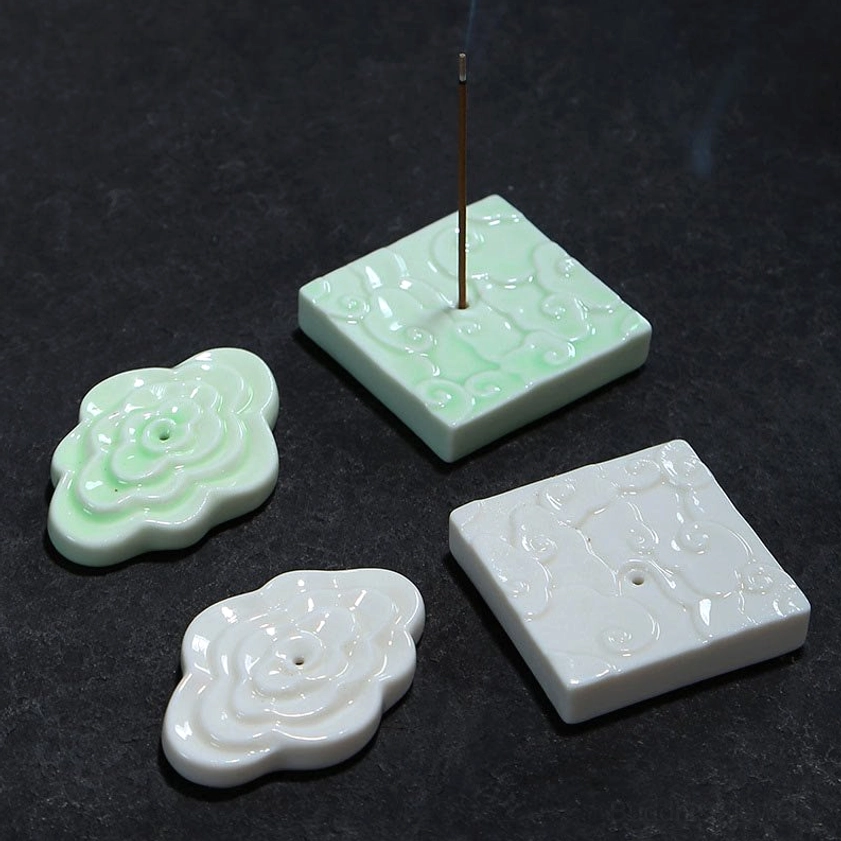 Top-down flat lay comparison of ceramic cloud incense holders in white and green variants on dark stone surface, displaying both color options with incense inserted