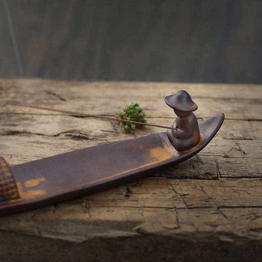 Brown ceramic boat incense holder photographed from elevated angle on rustic wooden surface with accent plant