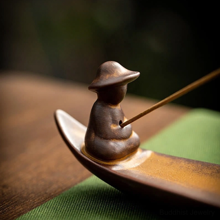 Close-up detail of handcrafted fisherman figurine with woven hat seated in ceramic boat incense holder
