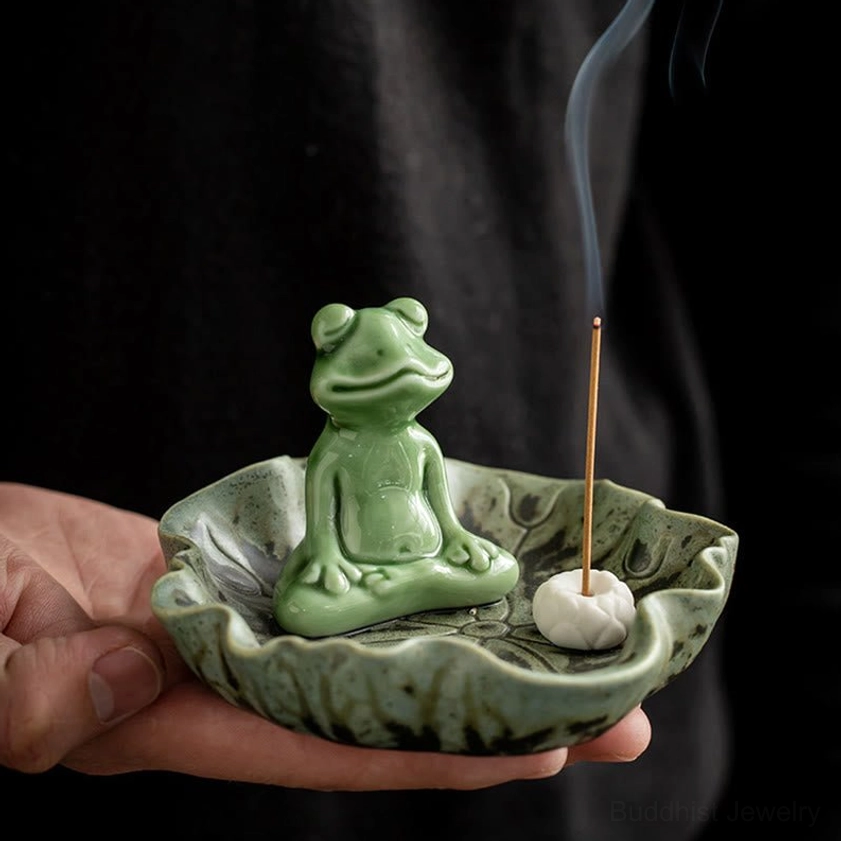 Buddhist frog ceramic incense holder held in hands with incense stick inserted, close-up detail view