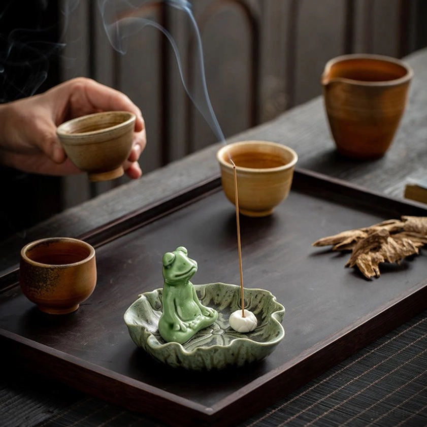 Frog ceramic incense burner on tea table with hand holding teacup and burning incense ambiance