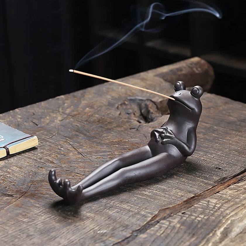 Handcrafted ceramic frog incense burner in praying position, three-quarter side view on rustic wooden table