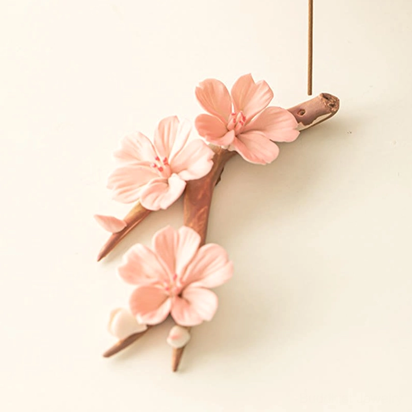 Natural branch-shaped ceramic incense burner with delicate pink blooms and mounted incense stick, minimalist white desk setting