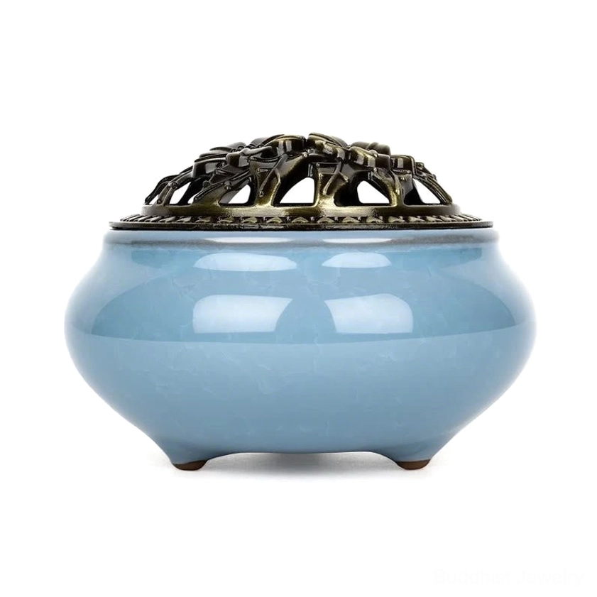 Ceramic incense burner with floral bronze hollow lid and three-footed base on white background