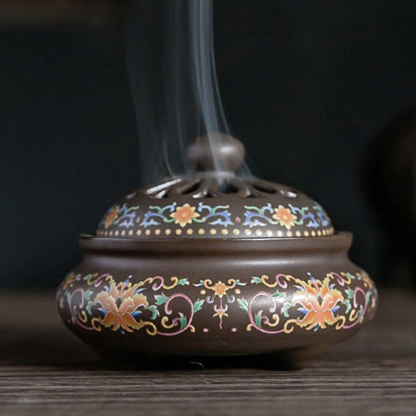 Side view of brown ceramic incense holder with intricate floral patterns, hollow carved lid, three-legged base design