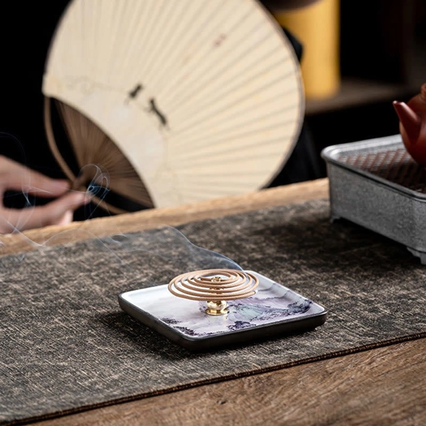 Coil incense burning in handcrafted ceramic burner tray on traditional tea table setup with smoke