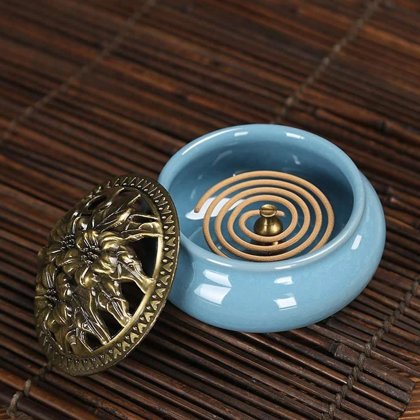 Ceramic incense burner with coil incense inside and decorative bronze lid on bamboo meditation mat