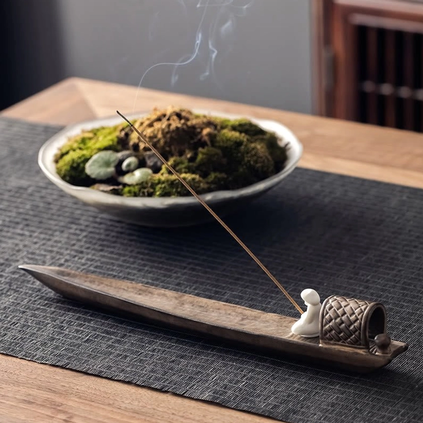 Low angle side view of handcrafted brown ceramic fishing boat incense holder with white figurine and rising incense smoke