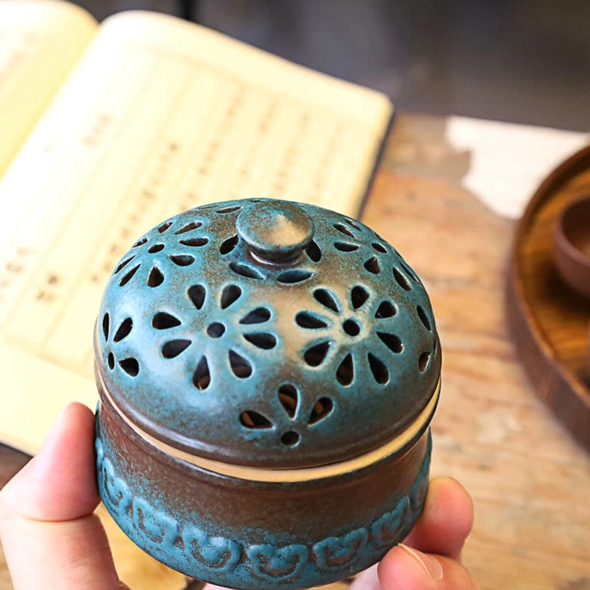 Handheld ceramic incense burner displayed at eye level showing heart-shaped embossed trim on base, held between fingers on wooden surface