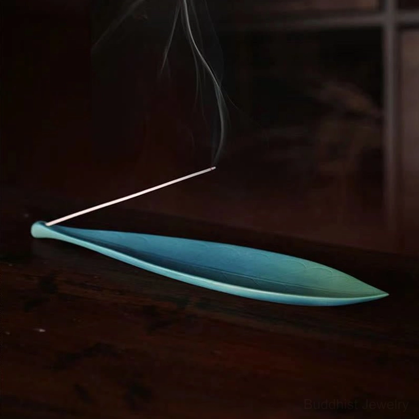 Ceramic leaf incense holder with lit incense stick and rising aromatic smoke