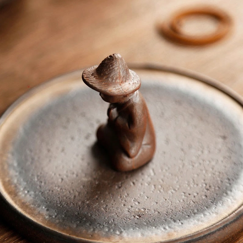 Close-up overhead view of kneeling monk ceramic incense burner tray with weathered brown glaze on dining table
