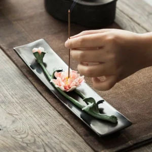 Handcrafted ceramic floral incense burner with pink lotus design on dark matte tray, overhead view on wooden table