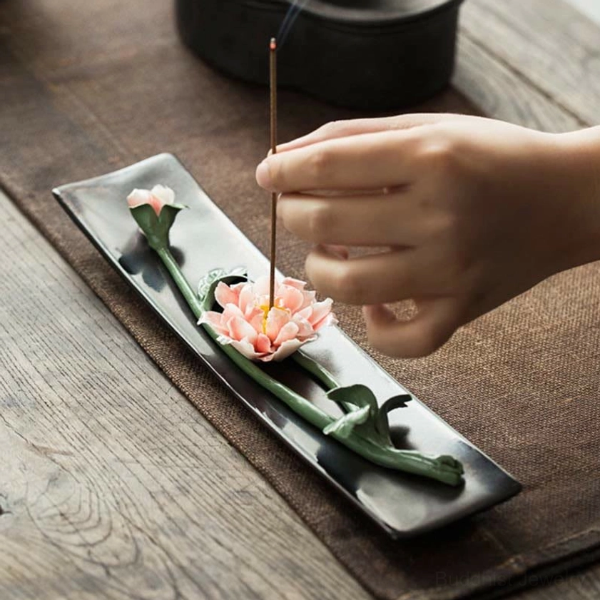 Handcrafted ceramic floral incense burner with pink lotus design on dark matte tray, overhead view on wooden table