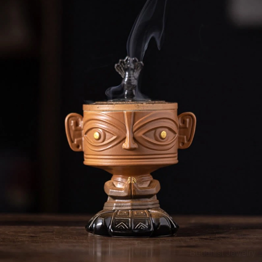 Ancient-inspired ceramic incense holder with carved relief face design, smoking incense on polished wooden table