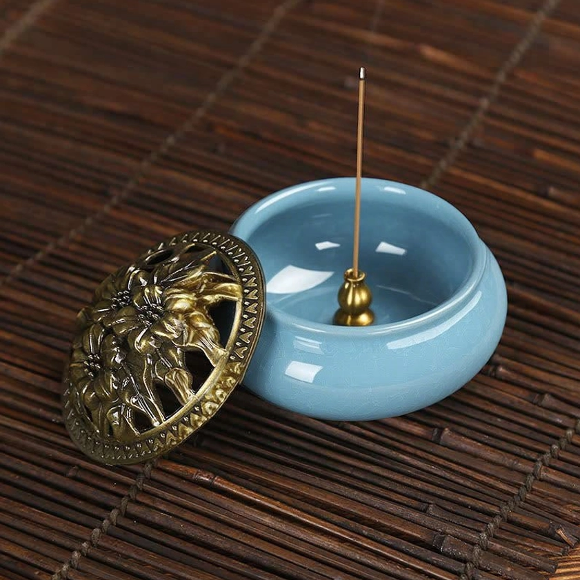 Ceramic incense burner with standing stick incense and bronze lid aside on bamboo mat