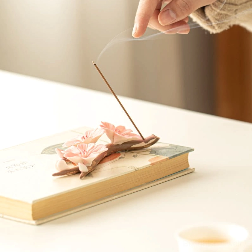 Burning incense in ceramic plum blossom holder with rising fragrant smoke, low side view with soft warm lighting