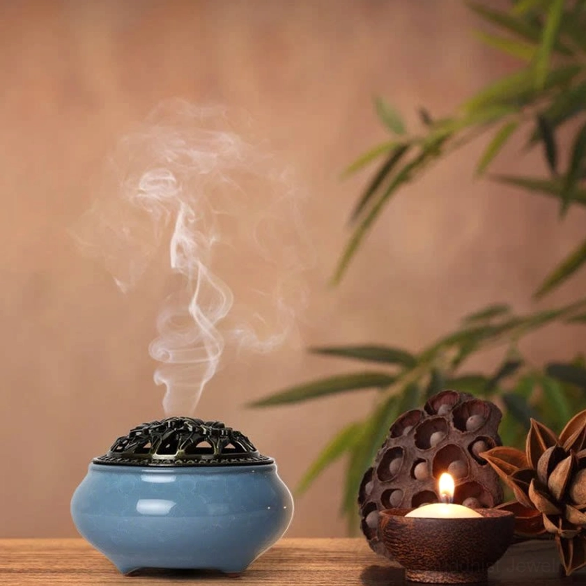 Ceramic incense burner in zen meditation setting with candle and decorative plants, showing spiritual ambiance