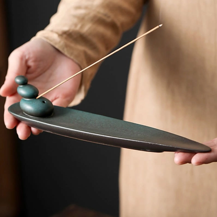 Close-up handheld view of ceramic incense holder with stacked stone motif holding single incense stick indoor