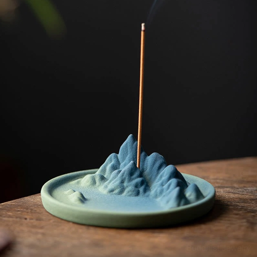 Buddhist ceramic backflow incense burner front view displaying mountain landscape design and teal colored base rim