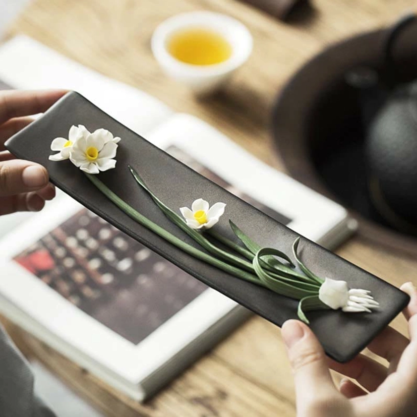 Handheld white daisy ceramic incense holder lifestyle shot, home tea table setting close-up