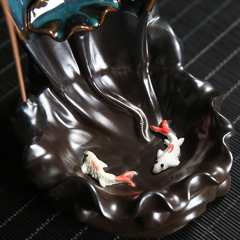 Decorative koi fish incense tray close-up showing dark brown ruffled ceramic base with two painted koi fish on wooden striped table