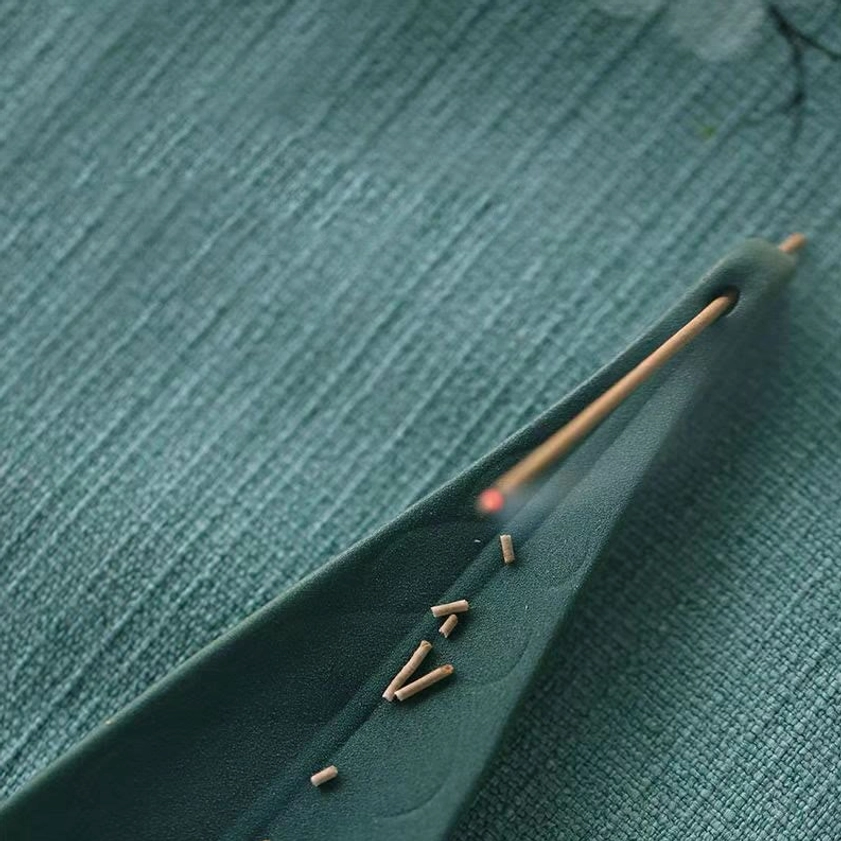 Dark green ceramic incense burner with lit incense stick and spare incense pieces