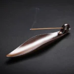 Ceramic leaf-shaped incense holder with lit incense stick and rising aromatic smoke for Buddhist meditation practice