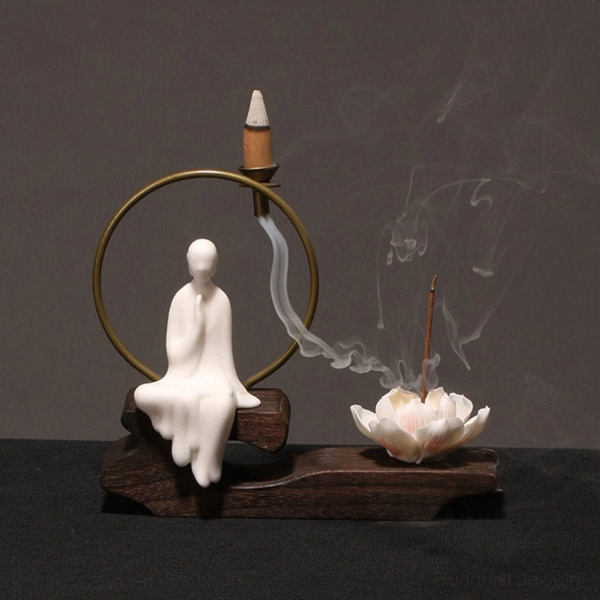 Handcrafted ceramic lotus backflow incense burner with seated white monk figurine and flowing incense smoke, featuring brass incense holder on wooden base